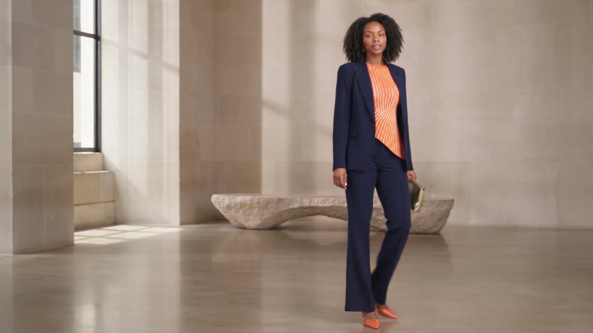Amara in a navy suit and orange top